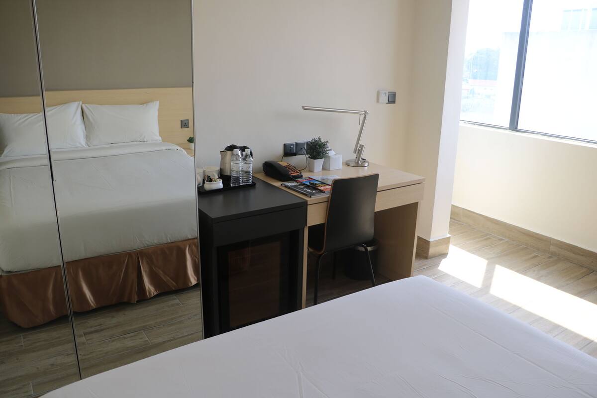 Habitación de hotel con cama, escritorio, silla, lámpara y ventana.