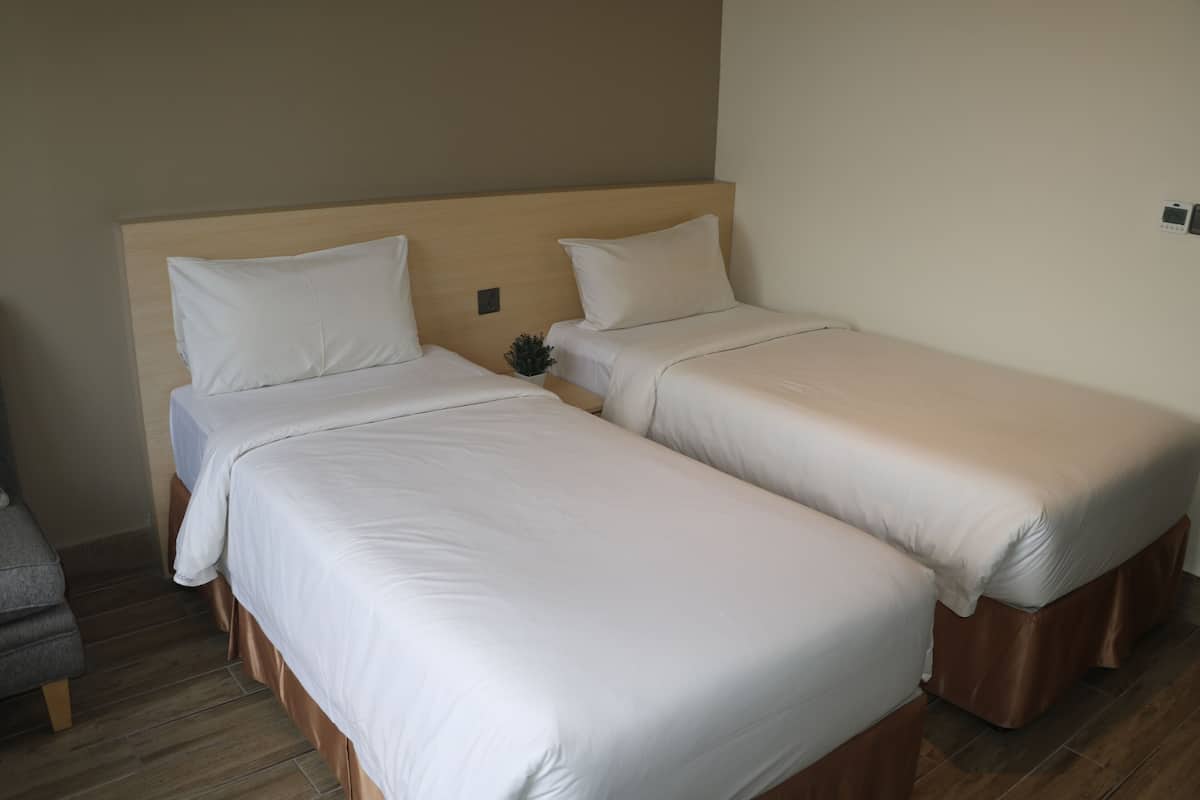 Habitación de hotel con dos camas individuales, cada una con ropa de cama blanca y cabeceros de madera.