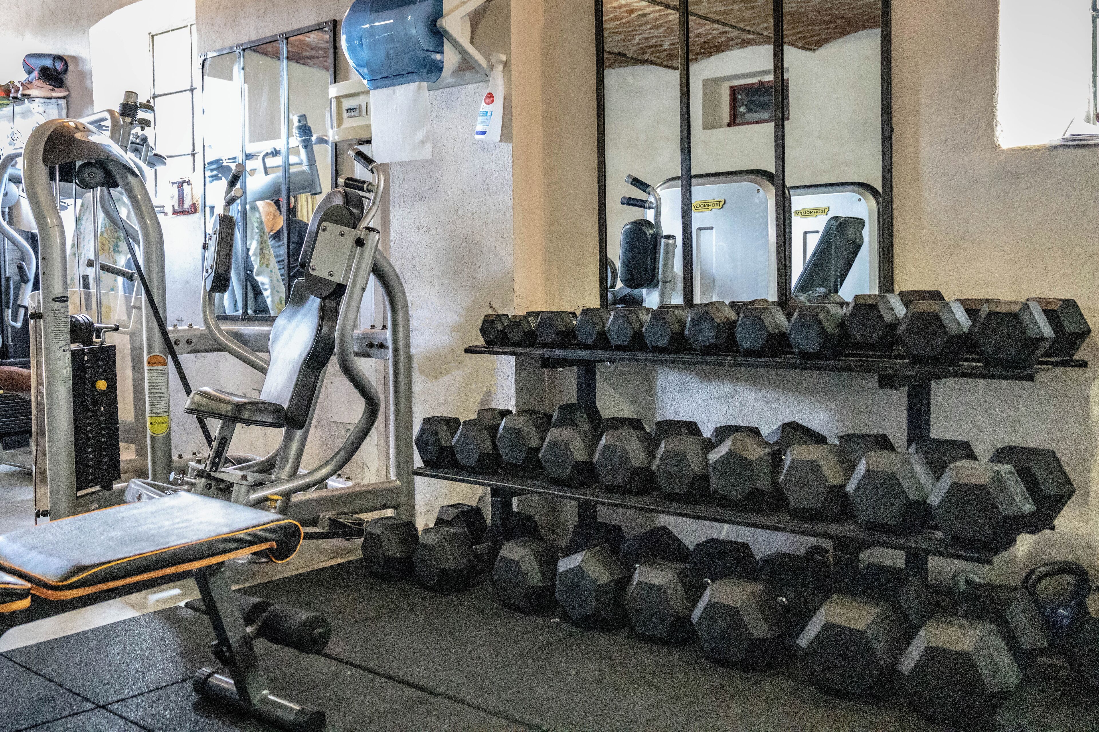 A gym with exercise equipment, including a bench, dumbbells, and a mirrored wall.