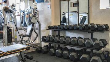 A gym with exercise equipment, including a bench, dumbbells, and a mirrored wall.