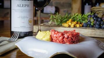 A bottle of Aleph wine, a glass of red wine, and a plate with a food item and some fruits.