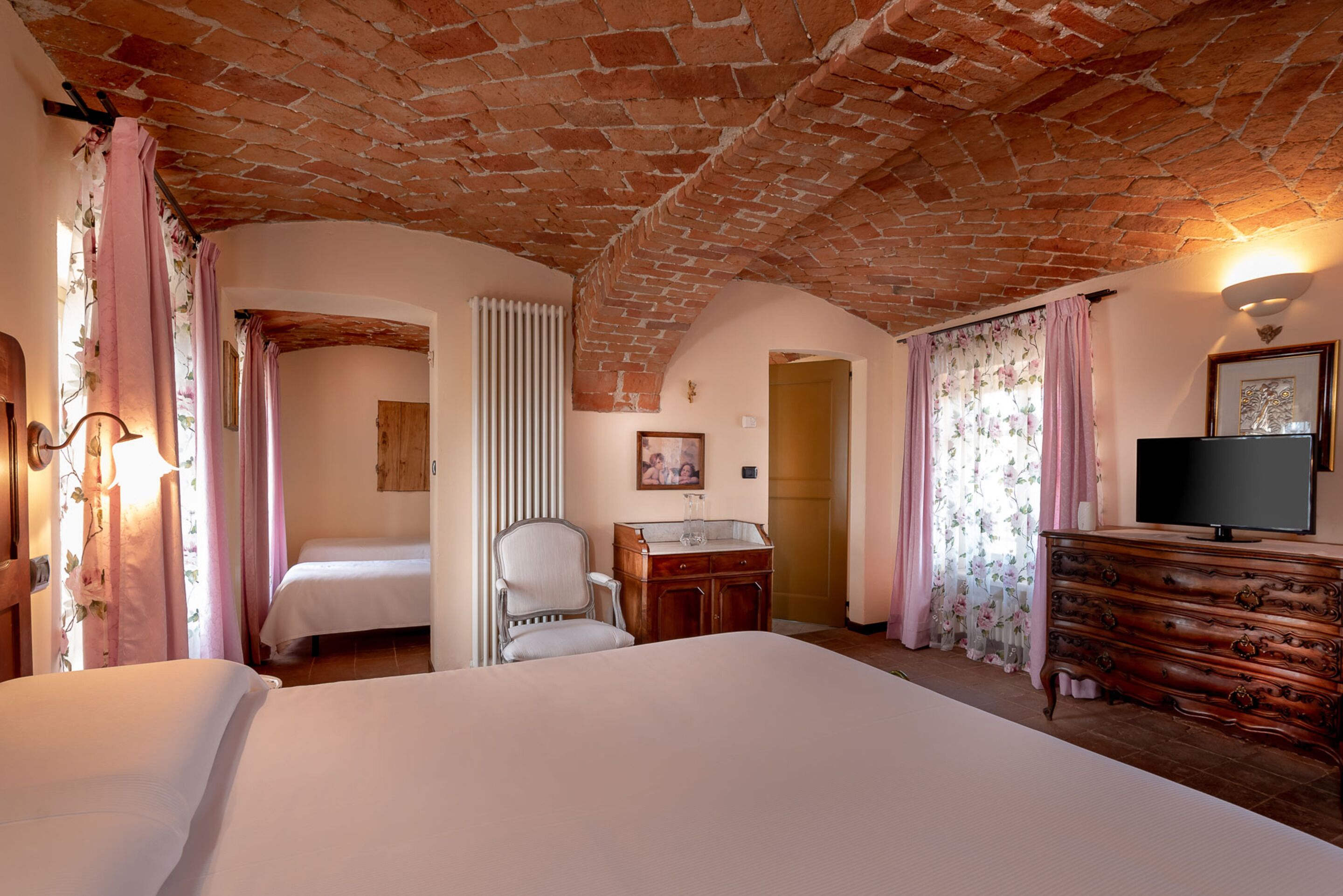 A hotel room with a brick ceiling, a bed, a dresser, a chair, and a television.