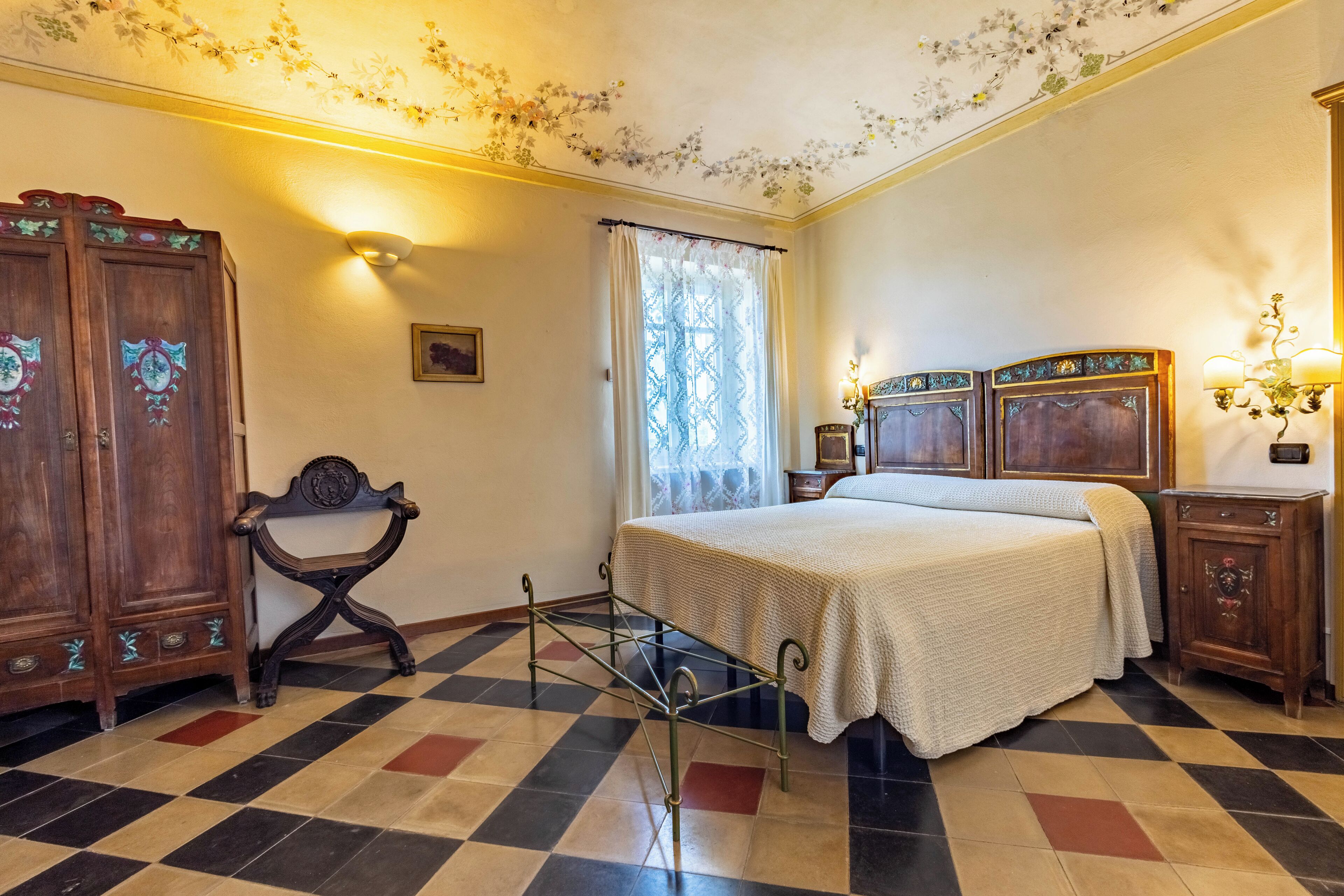 Een slaapkamer met een geruite vloer, een bed met een witte dekbedovertrek, een houten garderobe, een kleine tafel en een stoel.