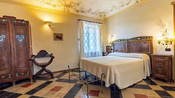 Een slaapkamer met een geruite vloer, een bed met een witte dekbedovertrek, een houten garderobe, een kleine tafel en een stoel.