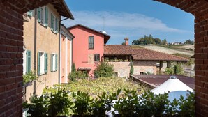 A courtyard with a brick archway, a red building with green shutters, and a stone building with a tiled roof. - San martino langhe (Clavesana)