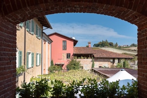 Un patio con un arco de ladrillo, un edificio rojo con contraventanas verdes y un edificio de piedra con tejado de baldosas.