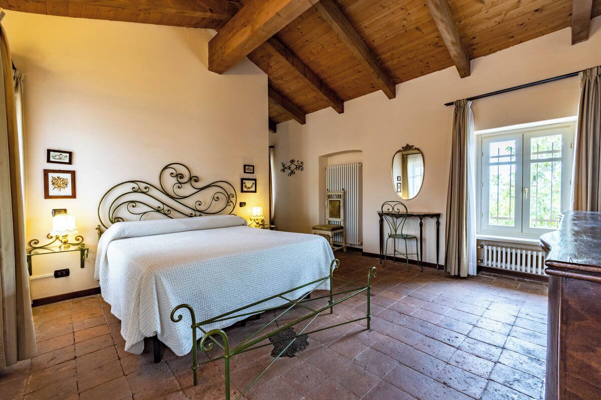 Un dormitorio con cama, vigas de madera, un radiador, un espejo y una ventana con cortinas.