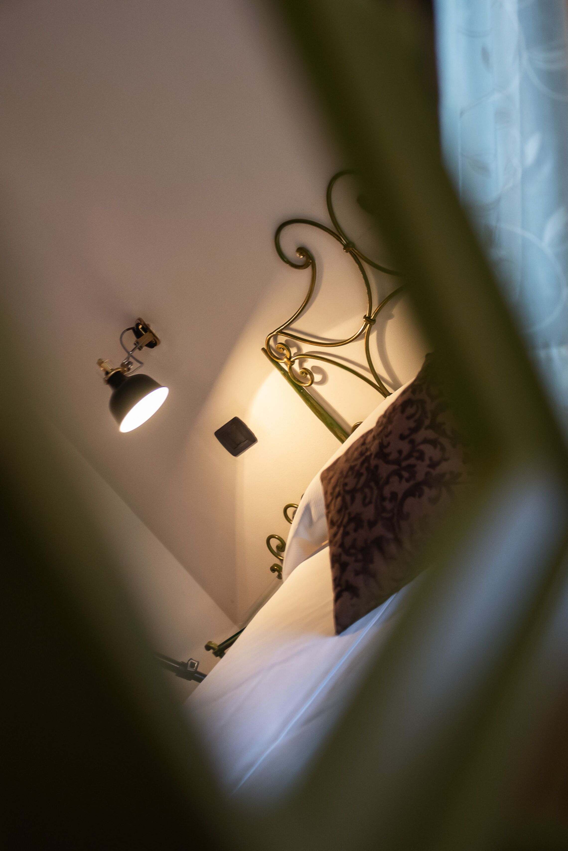 Un dormitorio con cama, una lámpara de pared y un cabecero metálico decorativo.