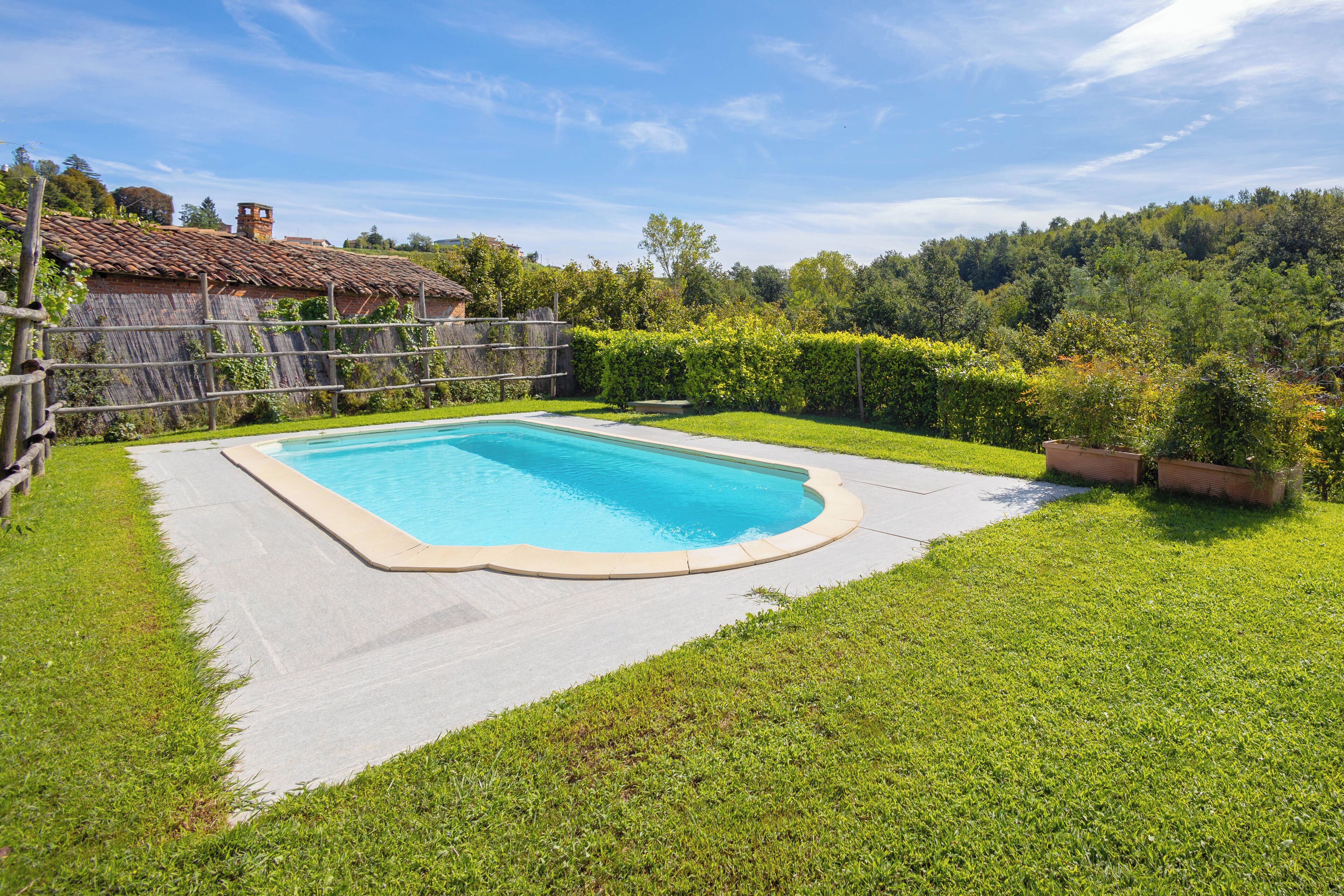 A rectangular swimming pool with a concrete deck, surrounded by well-maintained grass and a wooden fence.