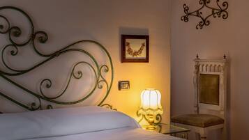 A neatly made bed with a green metal headboard, a bedside lamp, a framed picture on the wall, and a small white table with a chair.