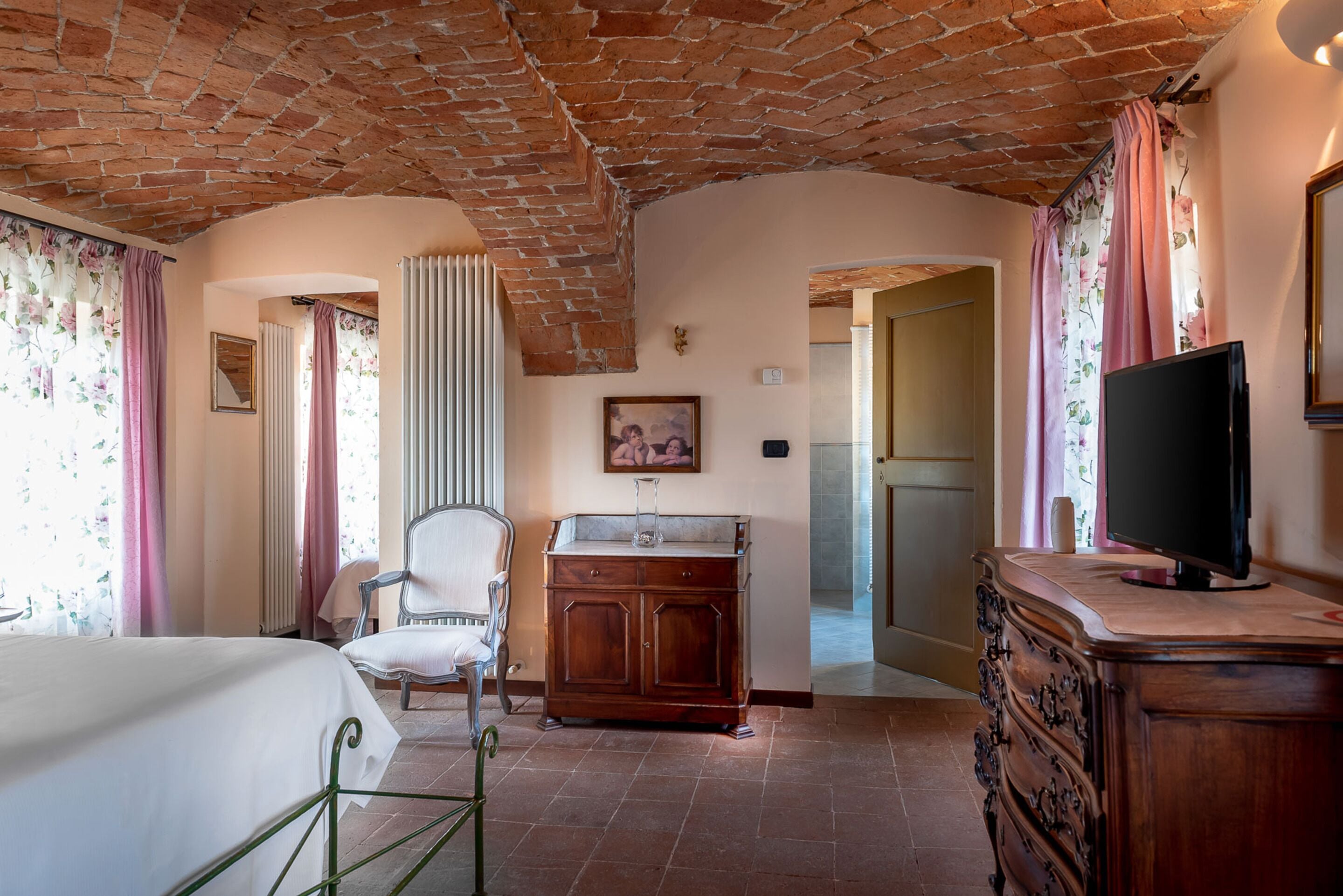 Une chambre d’hôtel avec un plafond en briques, un lit, une commode en bois, un téléviseur et une chaise.