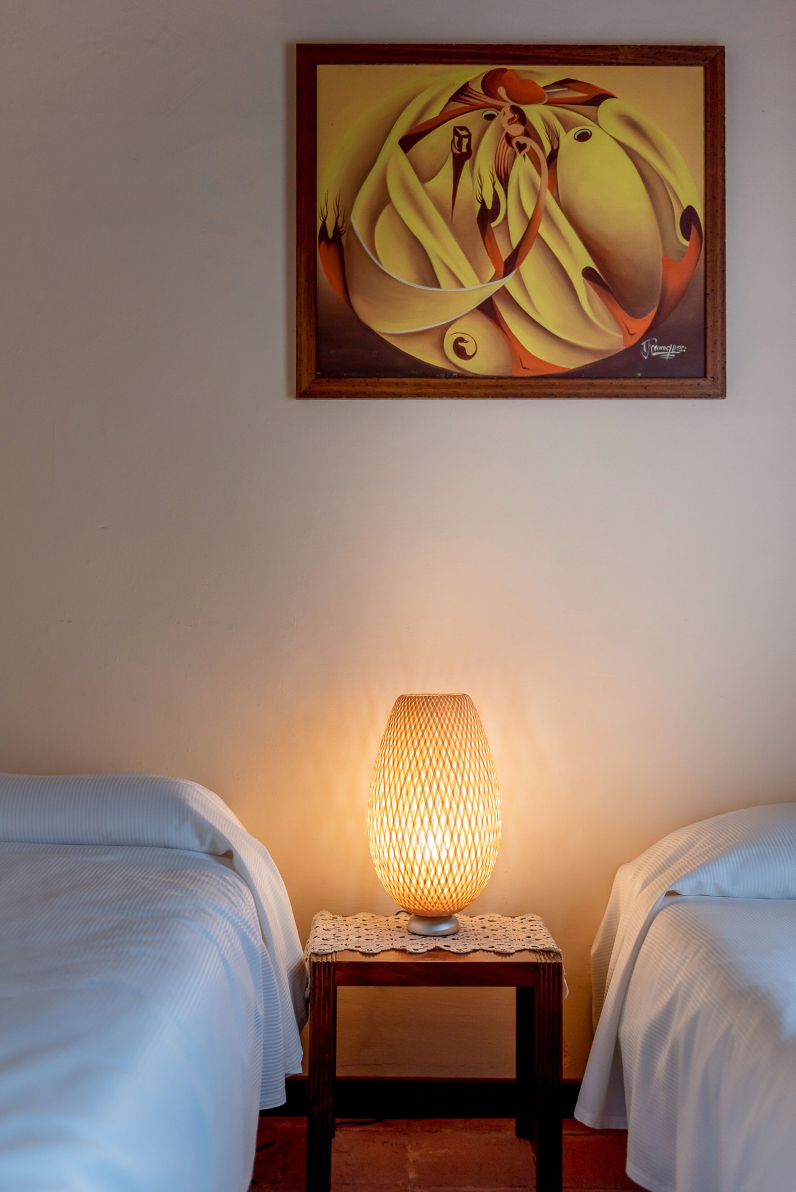 Una habitación con dos camas, una mesita de noche con lámpara y un cuadro en la pared.