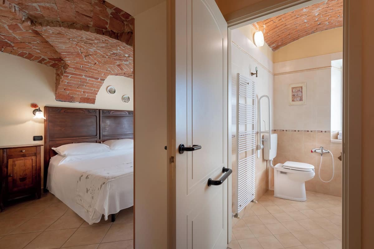 Un dormitorio con cabecera de madera, cama con sábanas blancas, mesita de noche y pared de ladrillo.