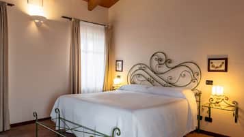 Una cama bien hecha con cabecera de metal, una mesita de noche con lámpara y una ventana con cortinas.