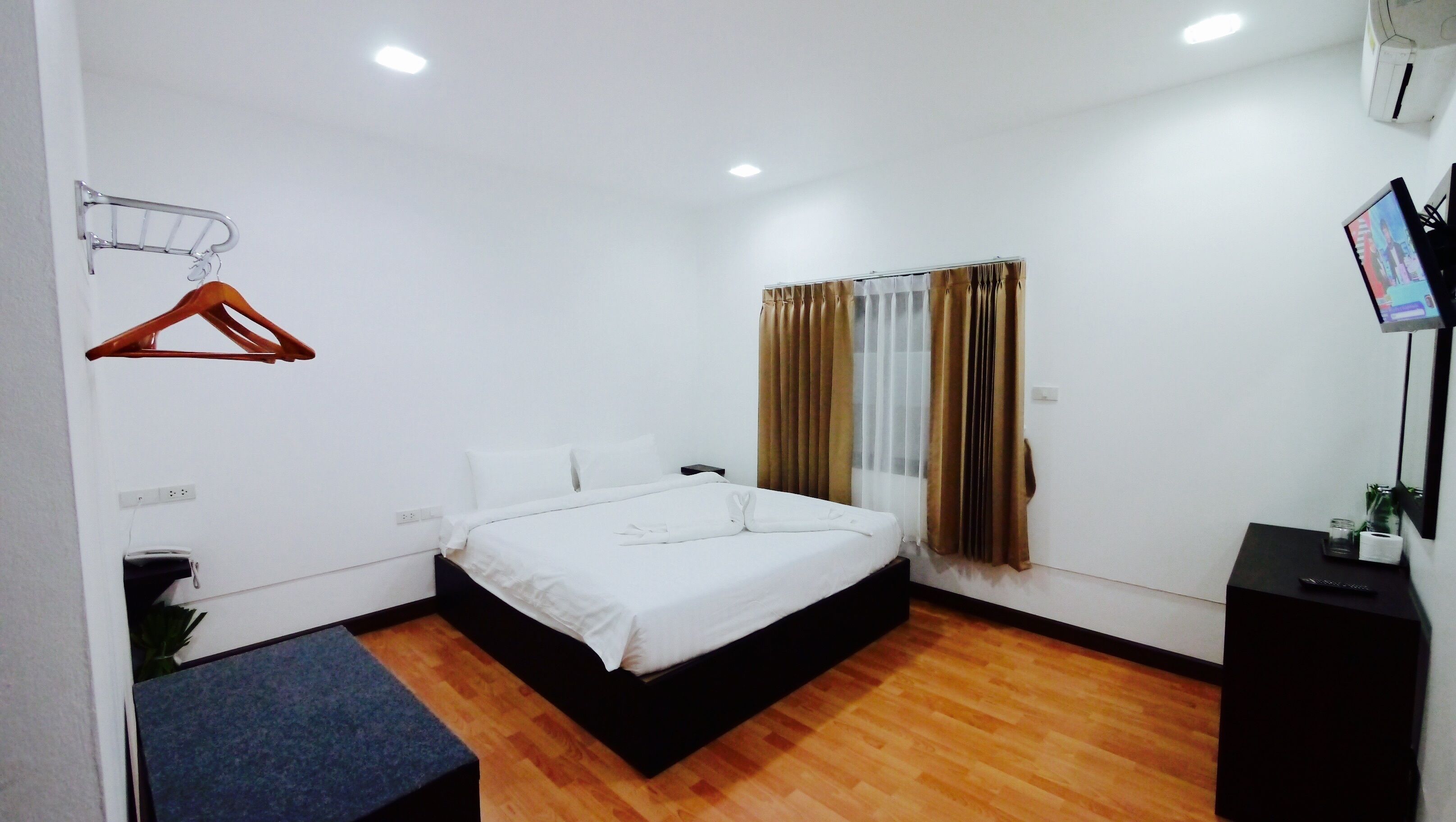 A hotel room with a single bed, a small desk, a TV, and a window with curtains.
