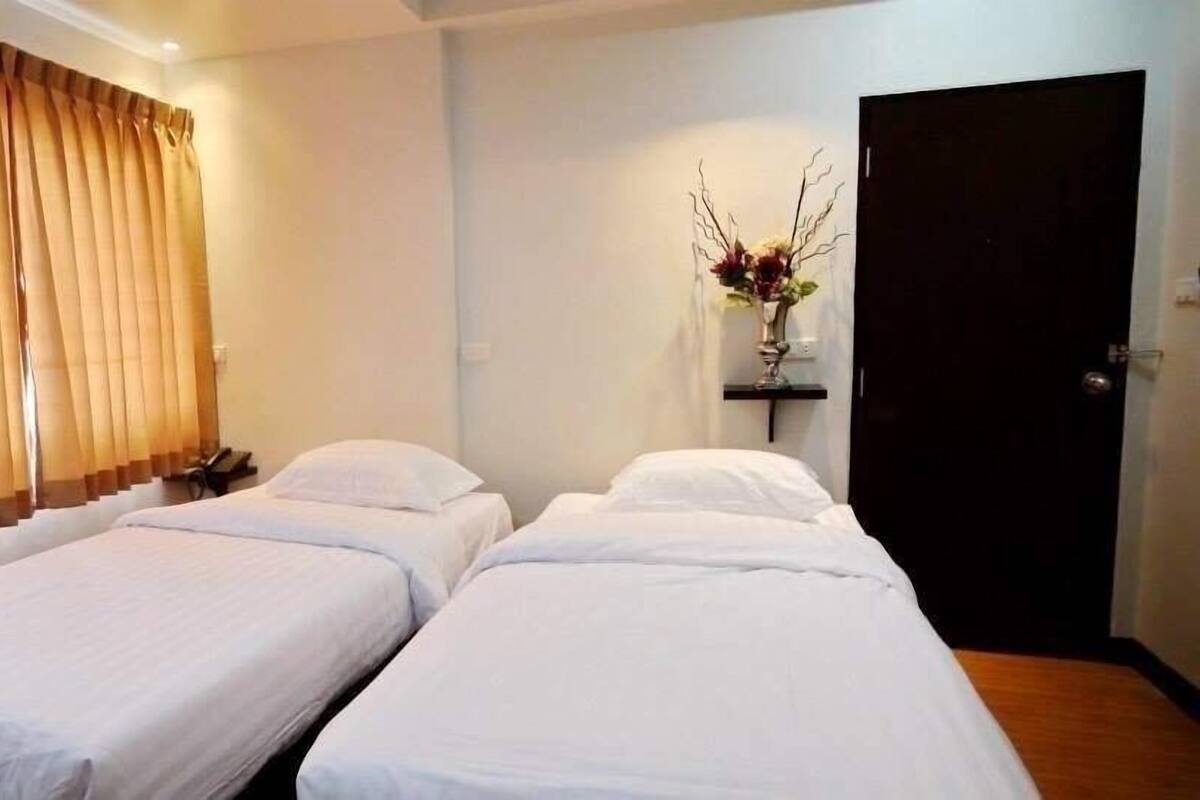 A room with two single beds, a dark door, and a window with vertical blinds.