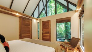 A bedroom with a large bed, wooden doors, and a view of trees through the windows. - Almonds and Corals Boutique Hotel (Cahuita)