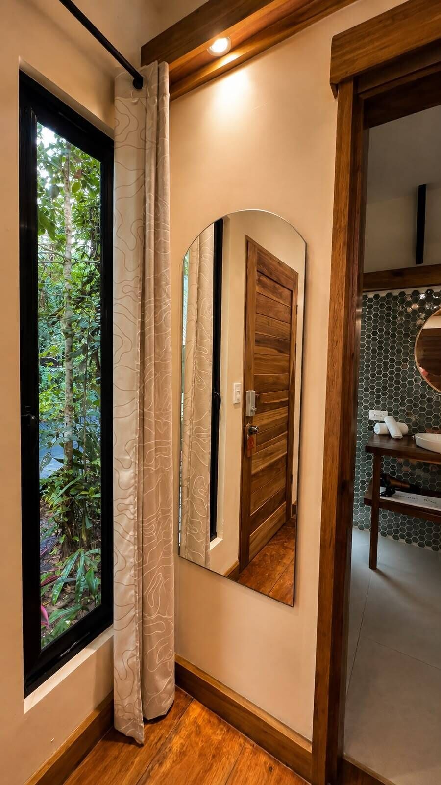 Een badkamer met een houten deur, een spiegel en een raam met gordijnen.