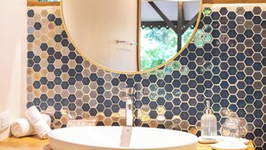 A bathroom with a round mirror, white sink, and a tiled hexagonal backsplash. - Almonds and Corals Boutique Hotel (Cahuita)