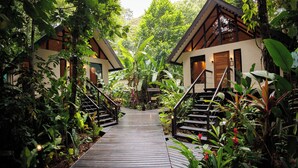 A wooden pathway leading to two guest cottages surrounded by lush greenery. - Almonds and Corals Boutique Hotel (Cahuita)