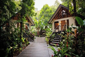 A wooden pathway leading to two guest cottages surrounded by lush greenery.