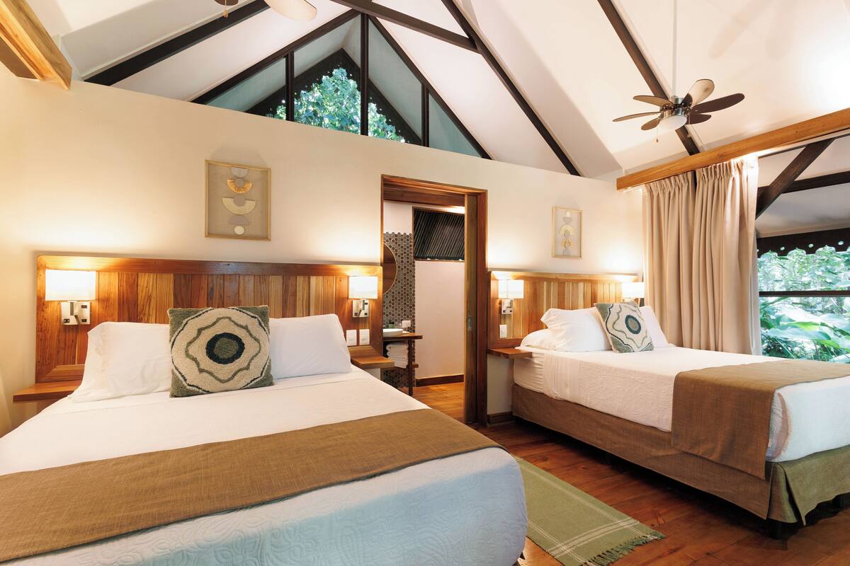 A hotel room with two beds, wooden headboards, and a ceiling fan.