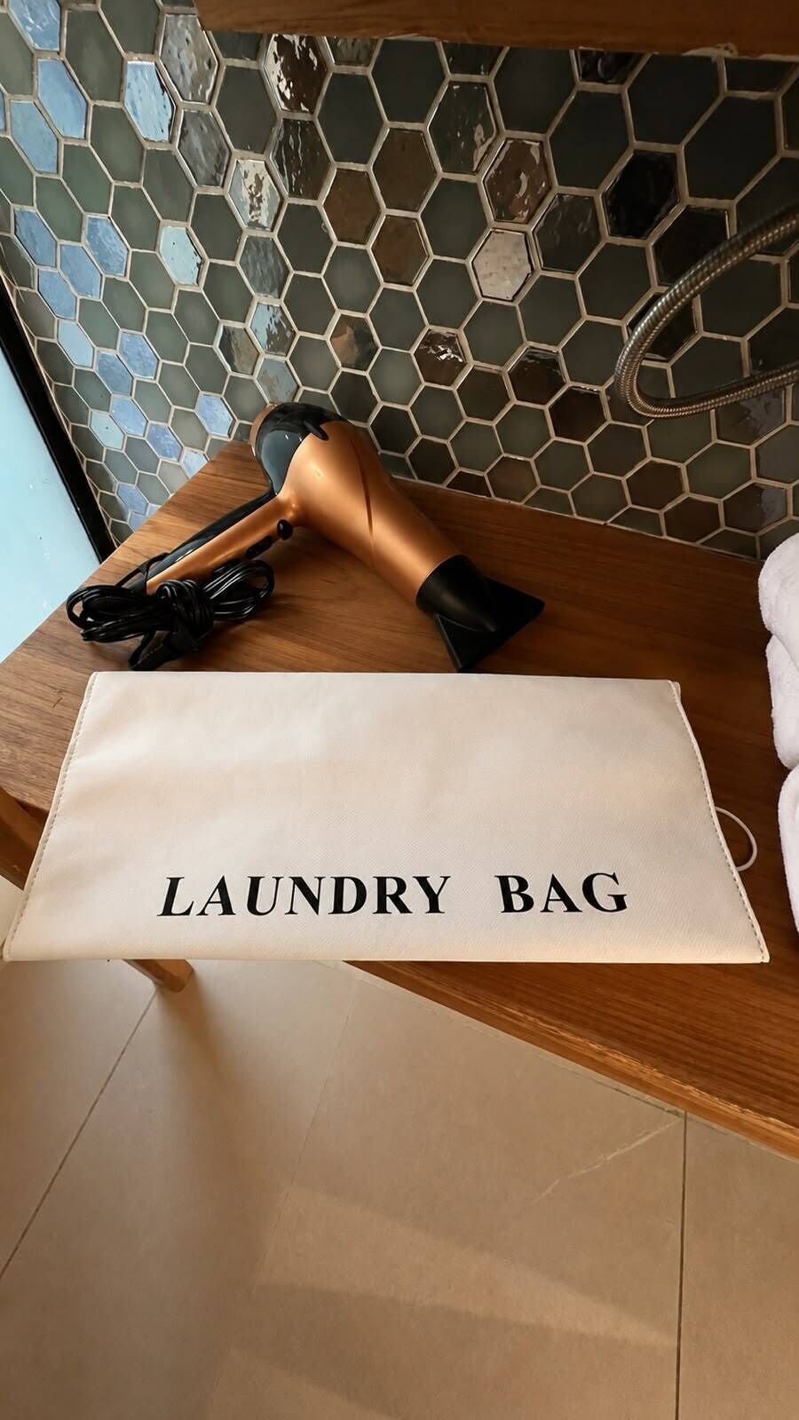 A wooden surface with a towel, a hairdryer, and a white bag labeled 'LAUNDRY BAG'.