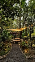 A garden pathway with a hammock, stone benches, and string lights.