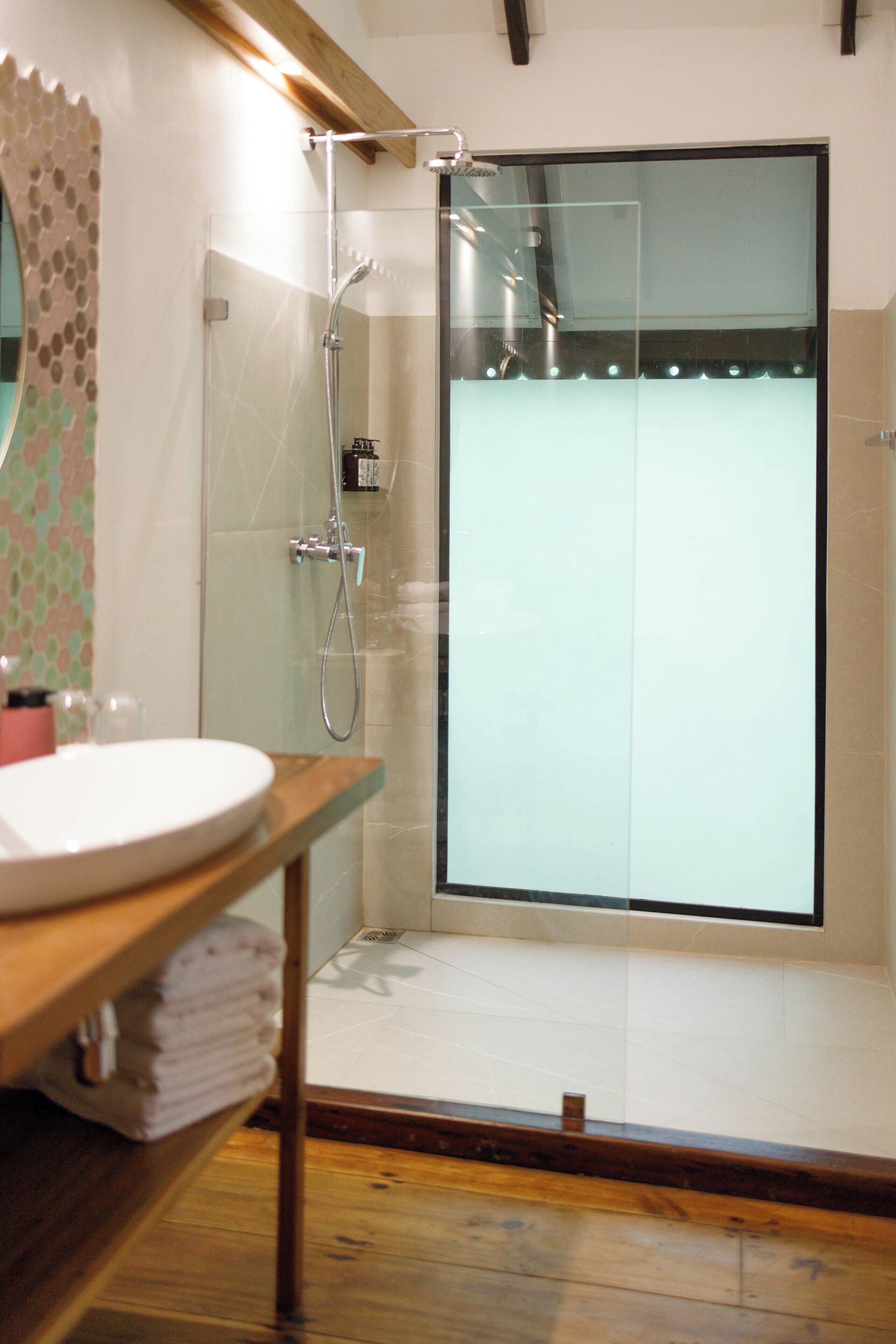 A modern bathroom with a glass-enclosed shower, a wooden vanity with a sink, and a tiled floor.