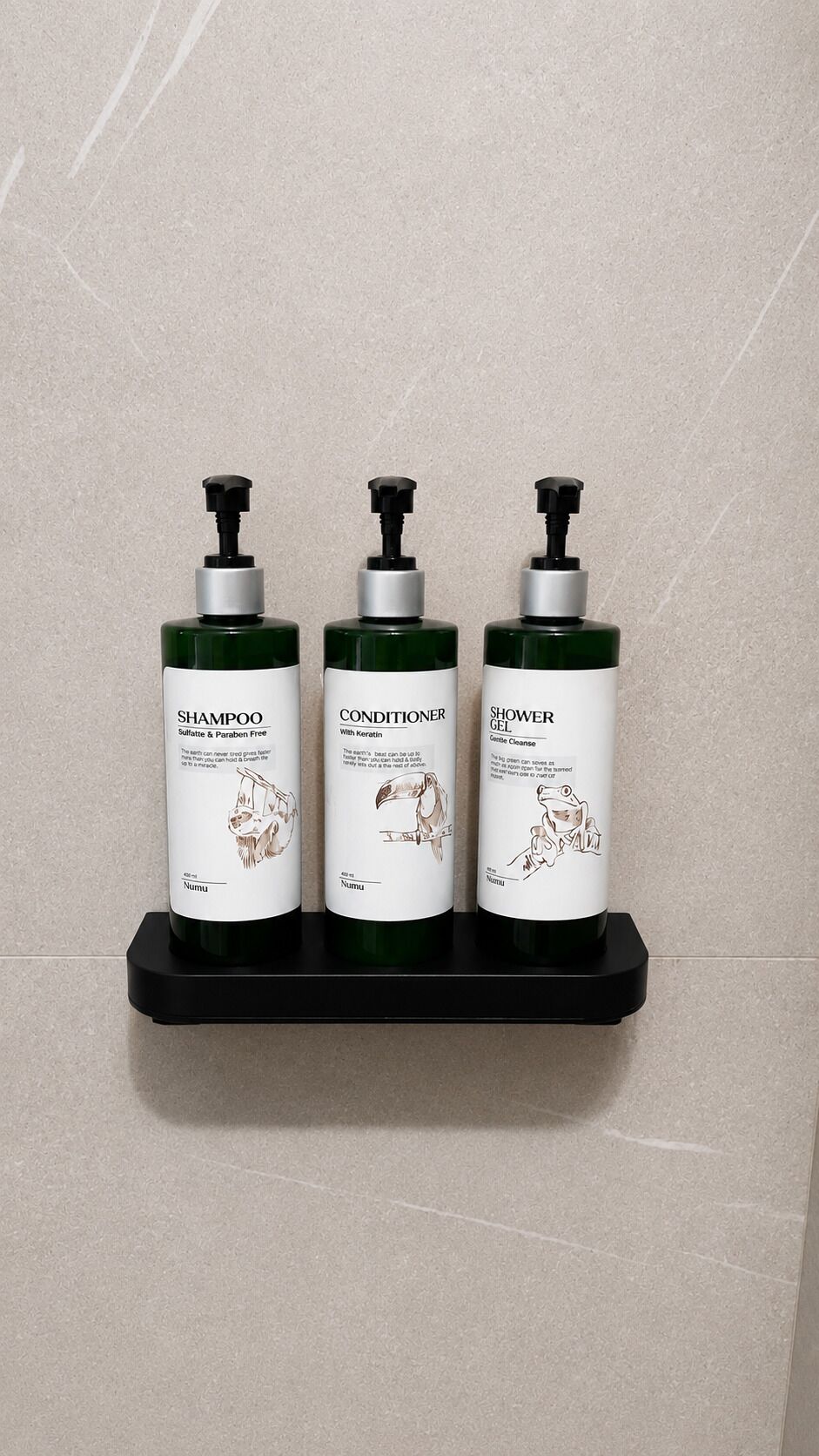 Três frascos de shampoo, condicionador e gel de banho sobre uma prateleira preta, em frente a uma parede revestida de azulejos.