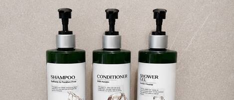 Três frascos de shampoo, condicionador e gel de banho sobre uma prateleira preta, em frente a uma parede revestida de azulejos.