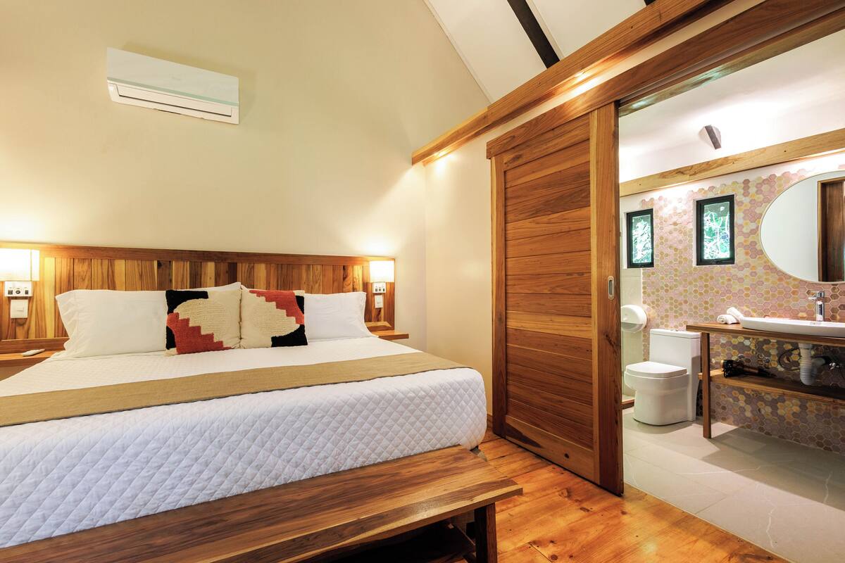 A bedroom with a wooden headboard, a large bed with white bedding, a bedside table, and a wooden bench.