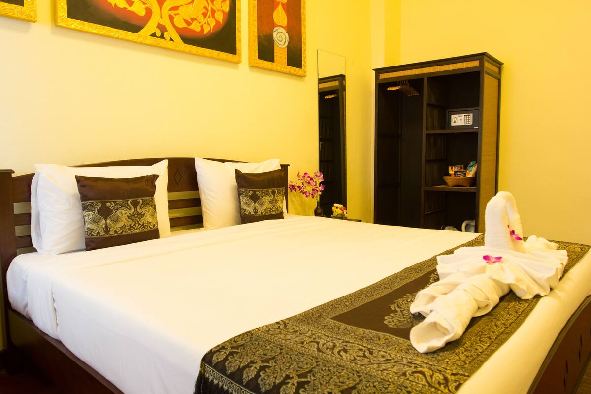A neatly made bed with white linens and a decorative headboard, a small vase with flowers, and a neatly folded towel on the bed.