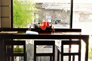 A wooden table with a window view of a street scene, including a motorcycle and a building with graffiti. - Sasima House (Chiang Mai)