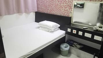 Una habitación de hotel con cama, un cubo de basura pequeño, un espejo y un aire acondicionado de pared.