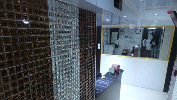 A modern interior with a reflective glass partition, a reception desk, and a mirror reflecting a person. - Yue Ka Hotel (Kowloon)