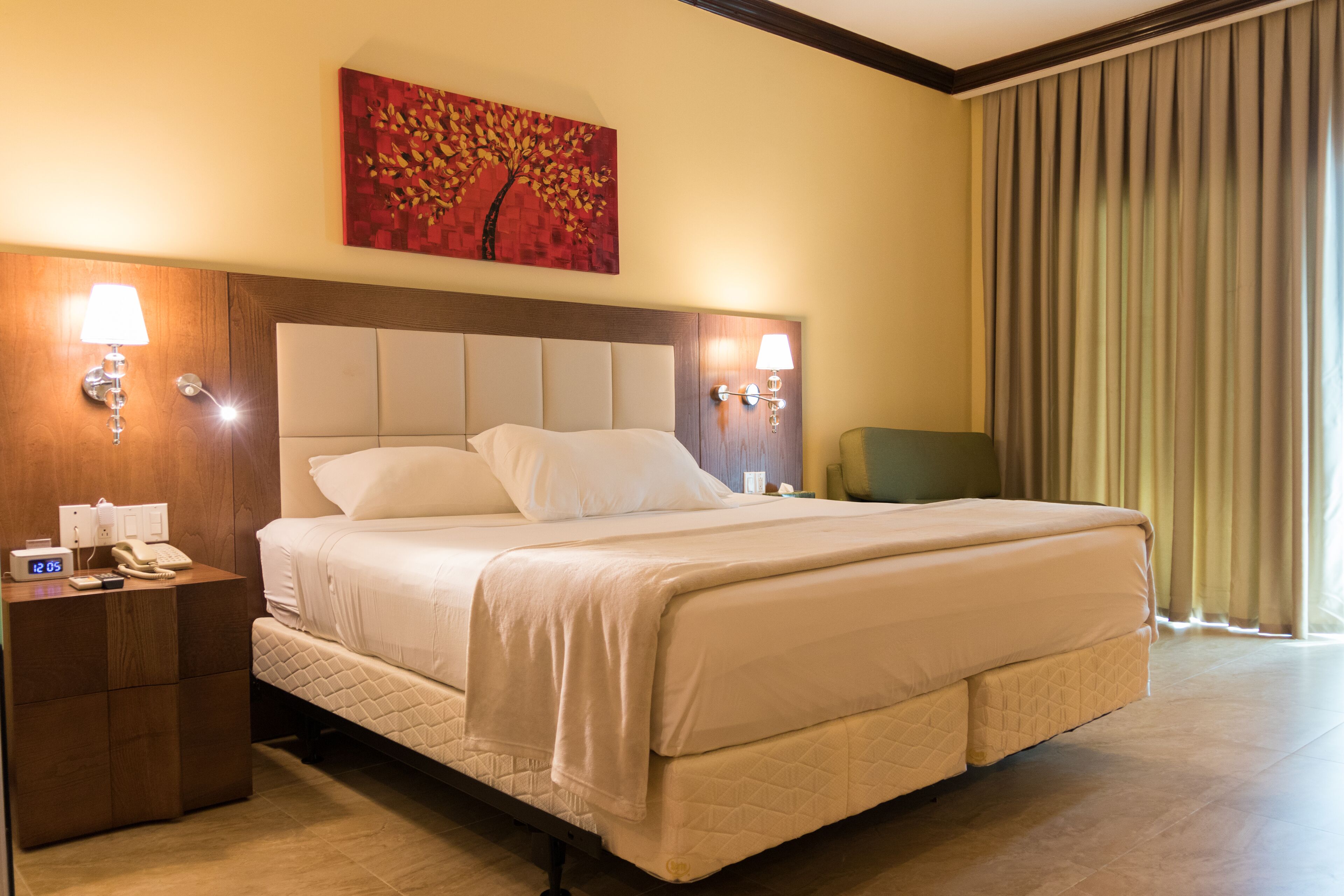 A hotel room with a large bed, bedside lamps, a nightstand with a phone, and a painting on the wall.