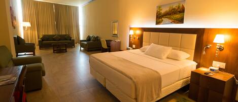 A hotel room with a large bed, a desk, a chair, a sofa, and a painting on the wall.