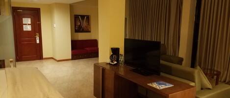 A hotel room with a bed, a TV, a coffee maker, a sofa, and a large window with curtains.