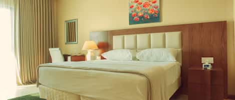 Habitación de hotel con una cama grande, una mesita de noche con lámpara, un cuadro de flores en la pared y una alfombra verde.