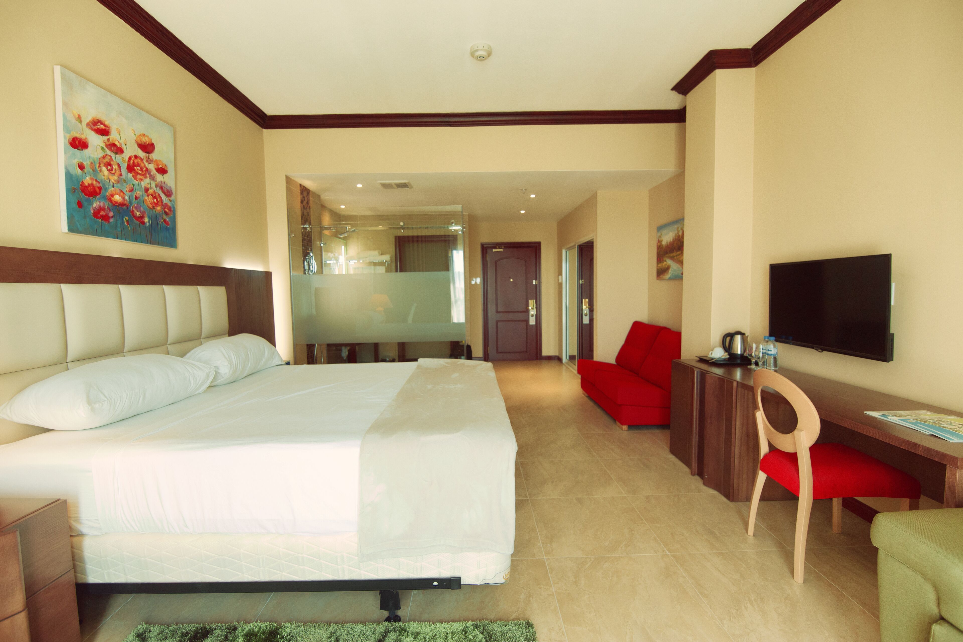 A hotel room with a bed, a desk, a TV, and a red chair.