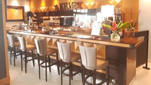 A bar area with a counter, bar stools, and a menu board. - Ramada Georgetown Princess Hotel (Georgetown)