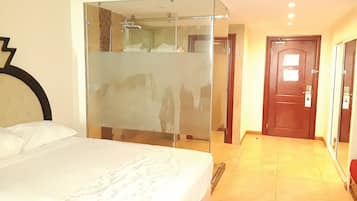 Una habitación de hotel con cama, una mampara de vidrio, una puerta de madera y piso de baldosas.