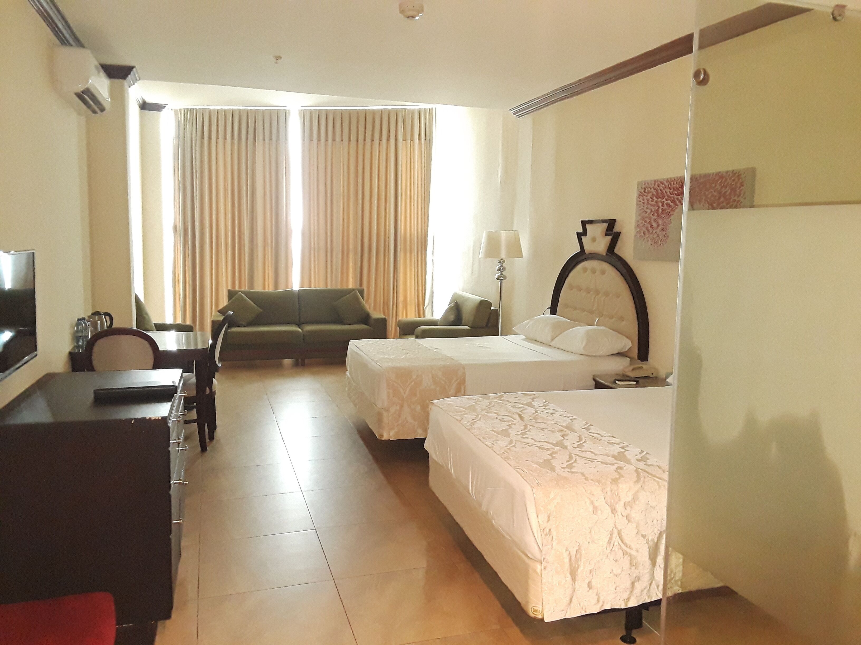 A hotel room with two beds, a desk, a television, and a sofa.