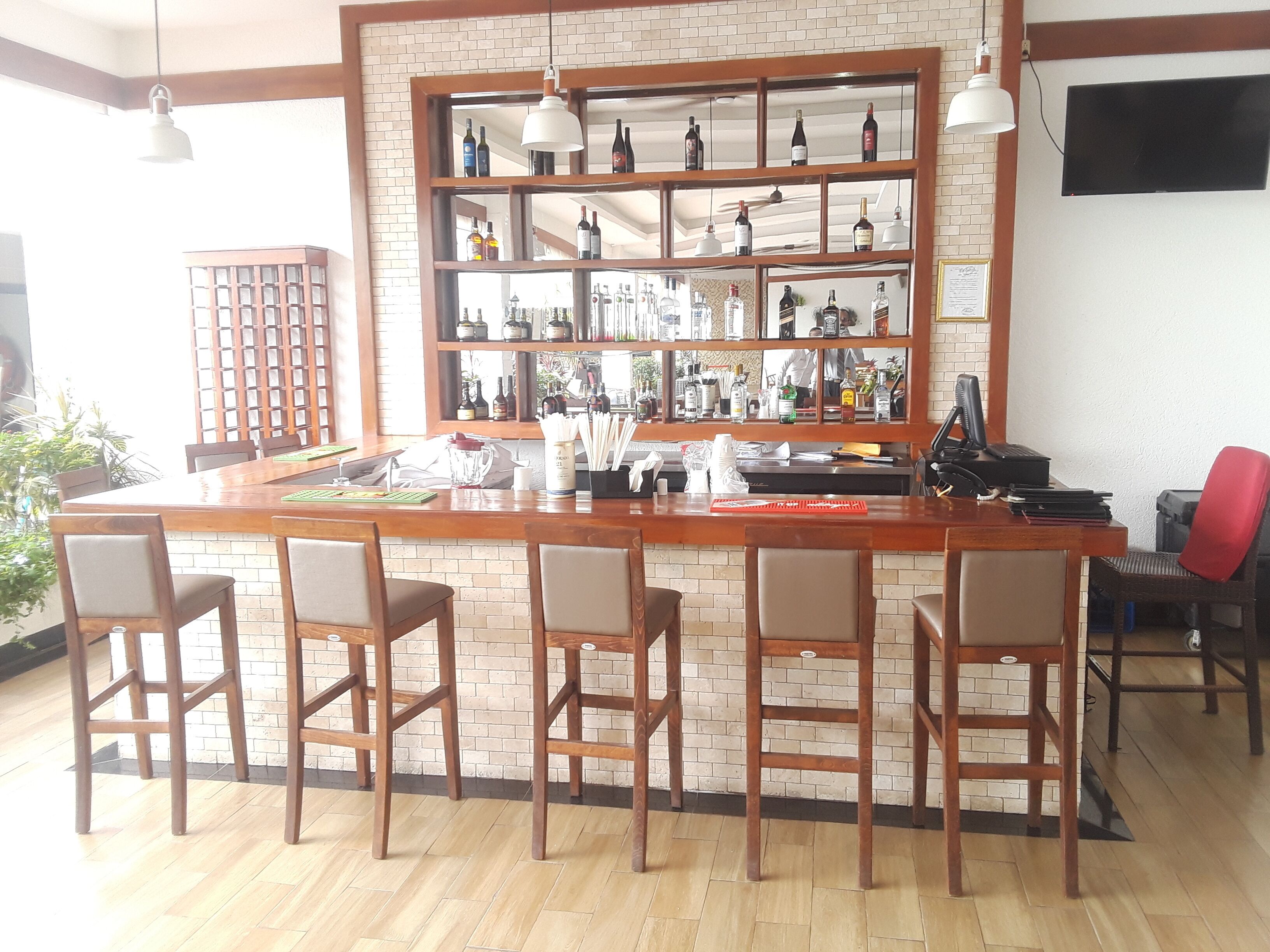 A bar area with a wooden counter, multiple stools, and a variety of bottles and glasses.