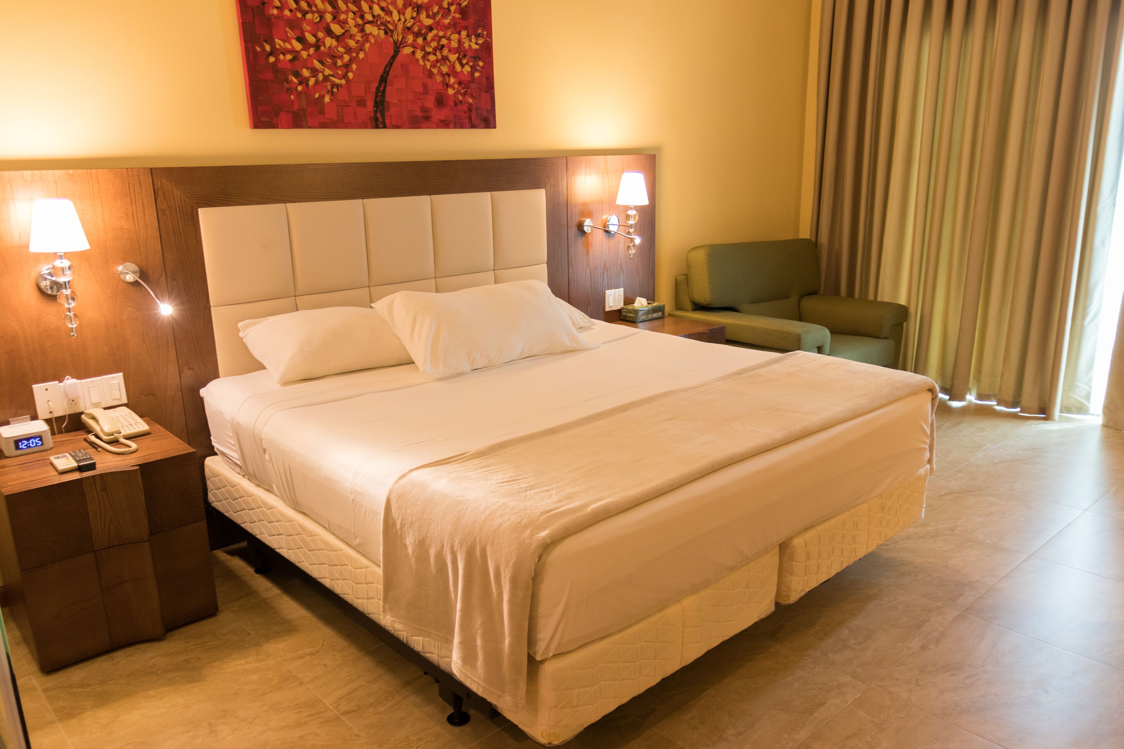 A hotel room with a large bed, a bedside table with a phone, a lamp, and a chair.