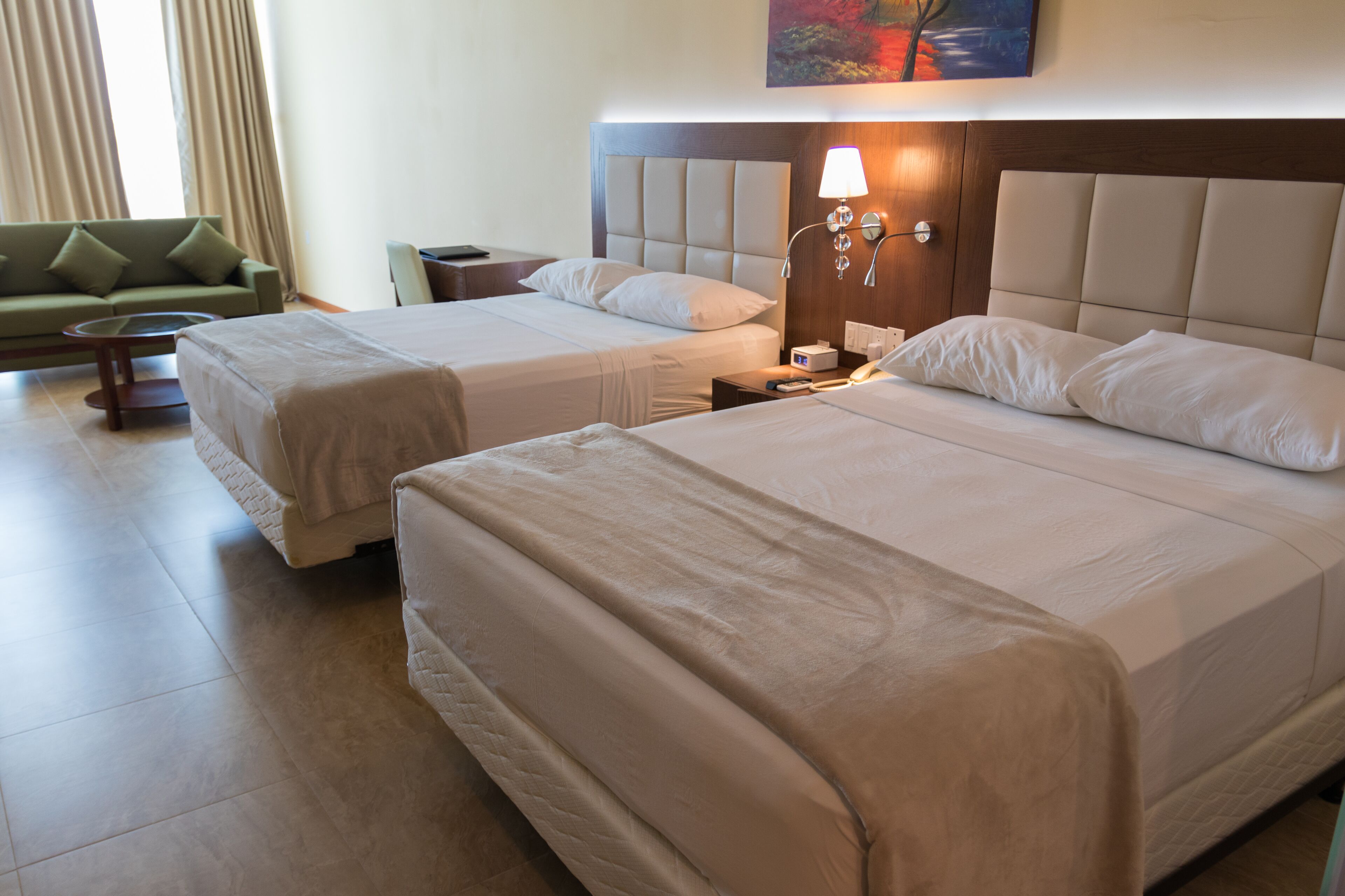 A hotel room with two beds, a green sofa, a bedside table, and a lamp.