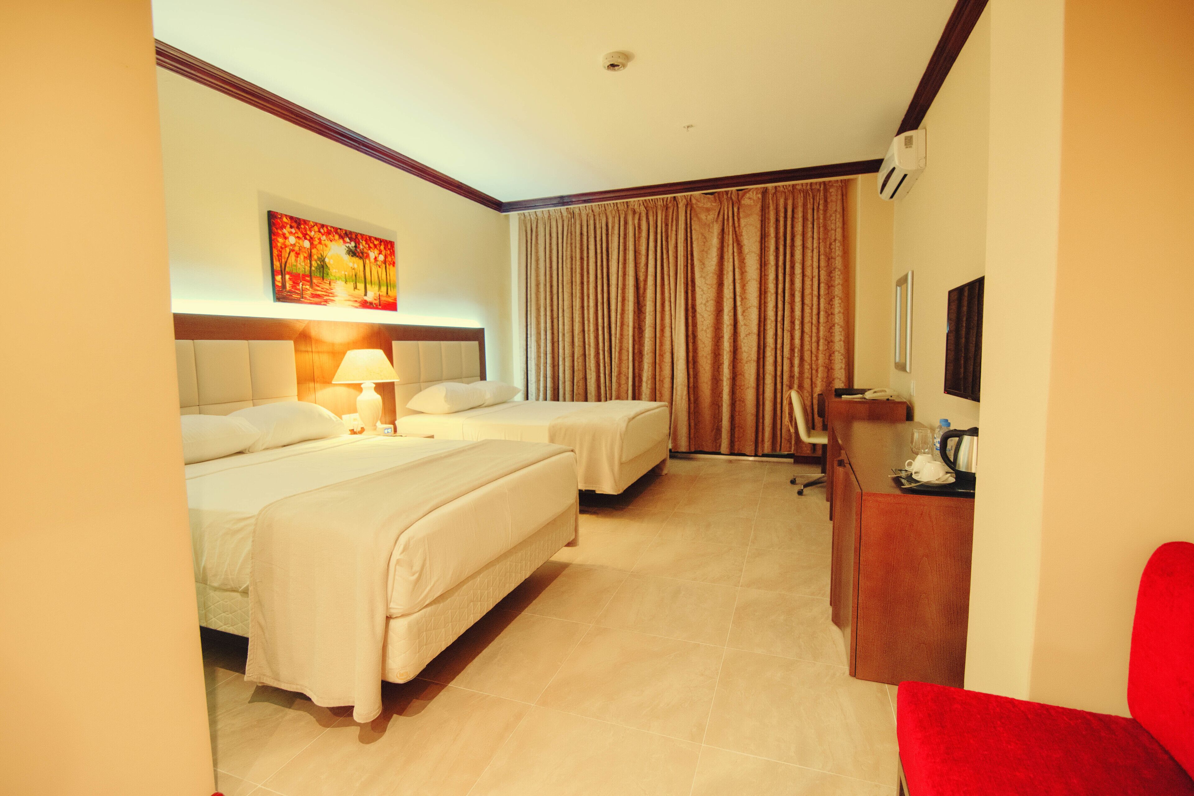 A hotel room with two beds, a desk, a chair, a lamp, and a painting on the wall.