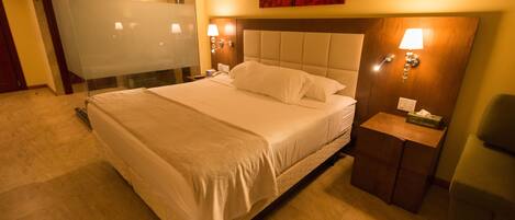 A hotel room with a large bed, a glass shower enclosure, and a wooden headboard.