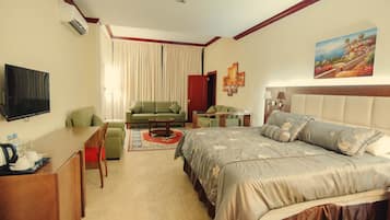 A hotel room with a bed, a sofa, a desk, a TV, and a painting on the wall.